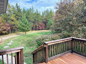 Une terrasse en bois, dotée d’une rambarde, qui offre une vue sur une cour verdoyante, avec des arbres et un ciel dégagé.