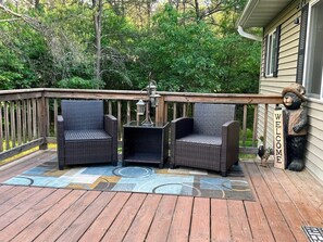 A wooden deck with two wicker chairs and a small table, a welcome sign, and a bear statue. - Secluded Woodland Retreat for 6 Near Wisconsin Dells, Lakes & ATV Trails (New Lisbon)