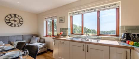 A modern kitchen with a large window, a dining area with a sofa, and a wall clock.