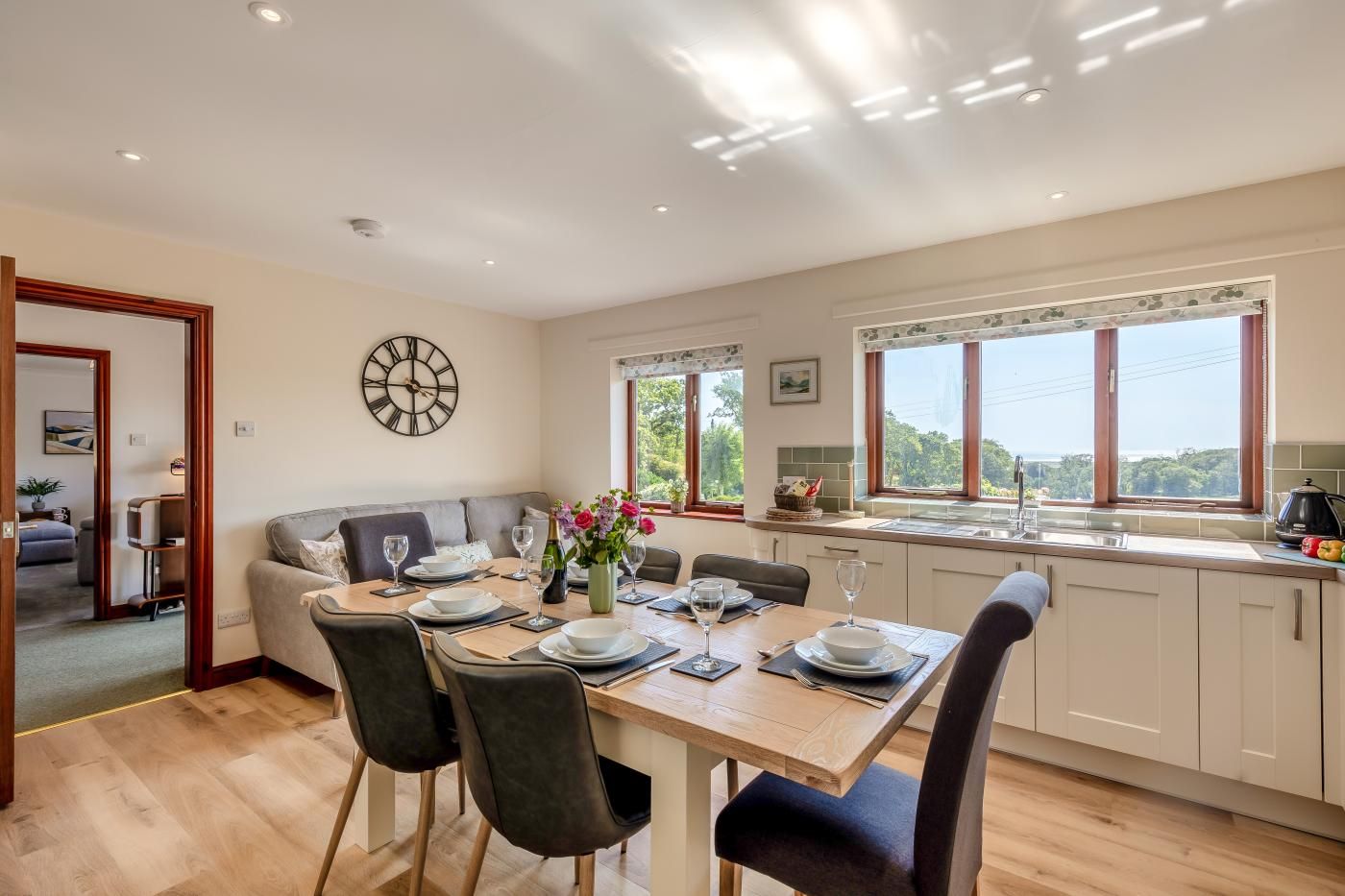 A modern kitchen with a dining area, large windows, and a view of greenery.