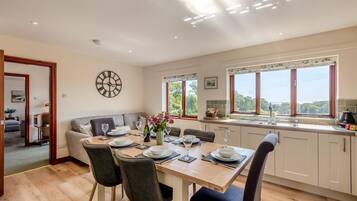 A modern kitchen with a dining area, large windows, and a view of greenery.
