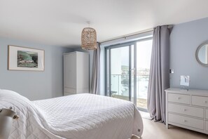 A bedroom with a bed, a wardrobe, a dresser, a mirror, and a balcony with a view. - 3 Bed in West Bay (oc-e42672) (West Bay)