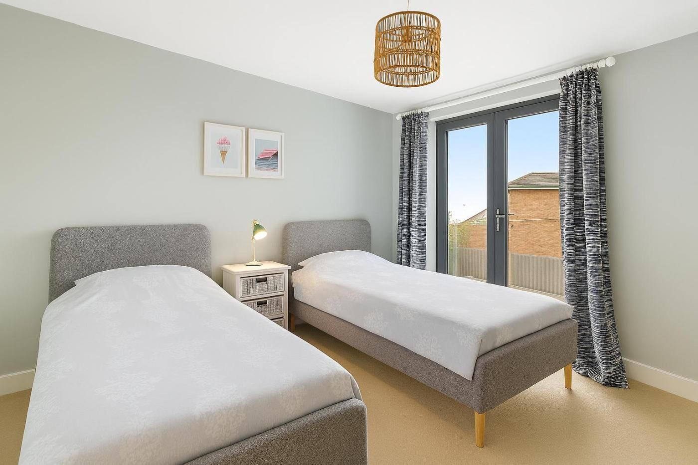 Un dormitorio con dos camas individuales, una mesita de noche con lámpara, una ventana con cortinas y vistas al exterior.