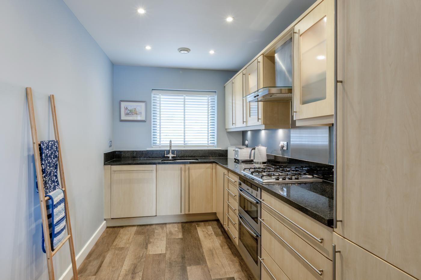 A modern kitchen with light wood cabinets, a stainless steel stove, and a black countertop.