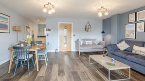 Un salon avec un canapé gris, une table basse et un coin repas comprenant une table et des chaises en bois.