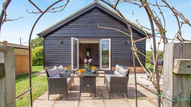 Eine Holzjagdhaus mit Terrasse, ausgestattet mit Korbmöbeln und einem Tisch mit Dekoration.