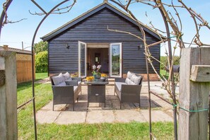 Eine Holzjagdhaus mit Terrasse, ausgestattet mit Korbmöbeln und einem Tisch mit Dekoration.