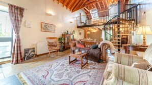 Un ampio soggiorno con soffitto in legno a volta, una scala e vista sull'esterno.