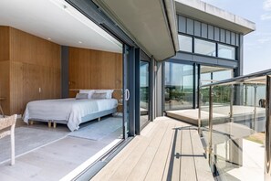 A modern bedroom with a large bed, a glass door leading to a balcony, and a view of the outdoors. - 7 Bed in Newquay (oc-s42829) (Newquay)