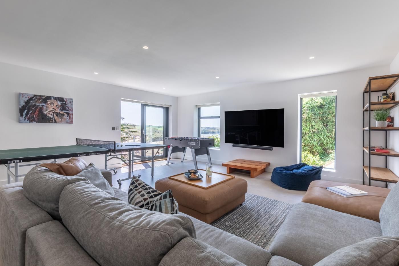 A modern living room with a ping pong table, a foosball table, a large flat-screen TV, and a comfortable seating area.