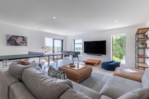 A modern living room with a ping pong table, a foosball table, a large flat-screen TV, and a comfortable seating area. - 7 Bed in Newquay (oc-s42829) (Newquay)