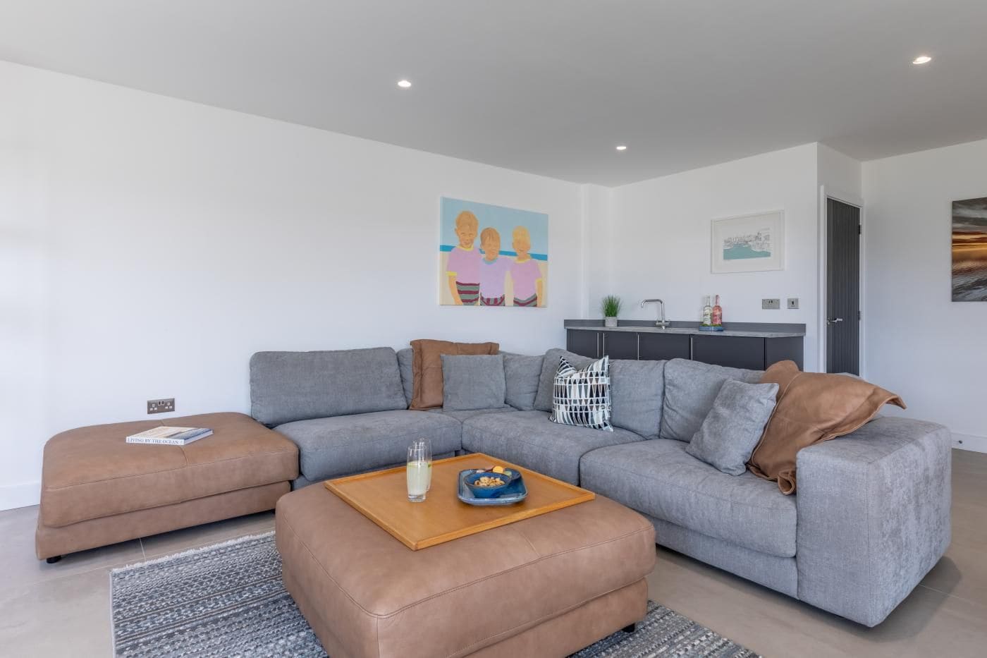 A modern living room with a grey sofa, a brown ottoman, and a wooden coffee table.