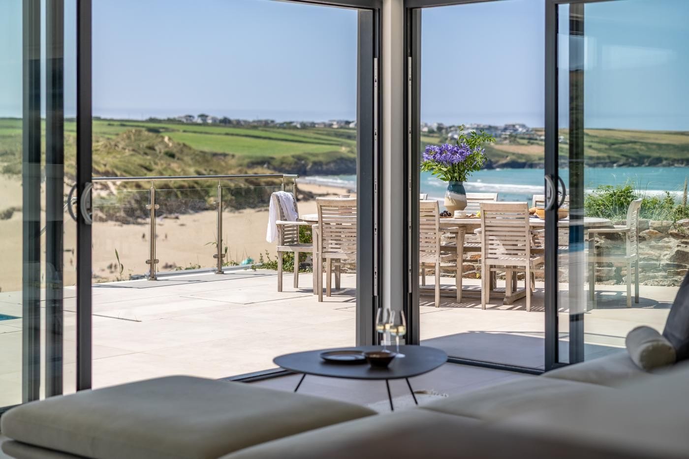 A modern living room with a large glass door leading to a balcony overlooking a beach.