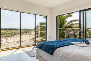 Ein Schlafzimmer mit einem großen Bett, Blick auf einen Strand und einem Balkon mit Palmen.