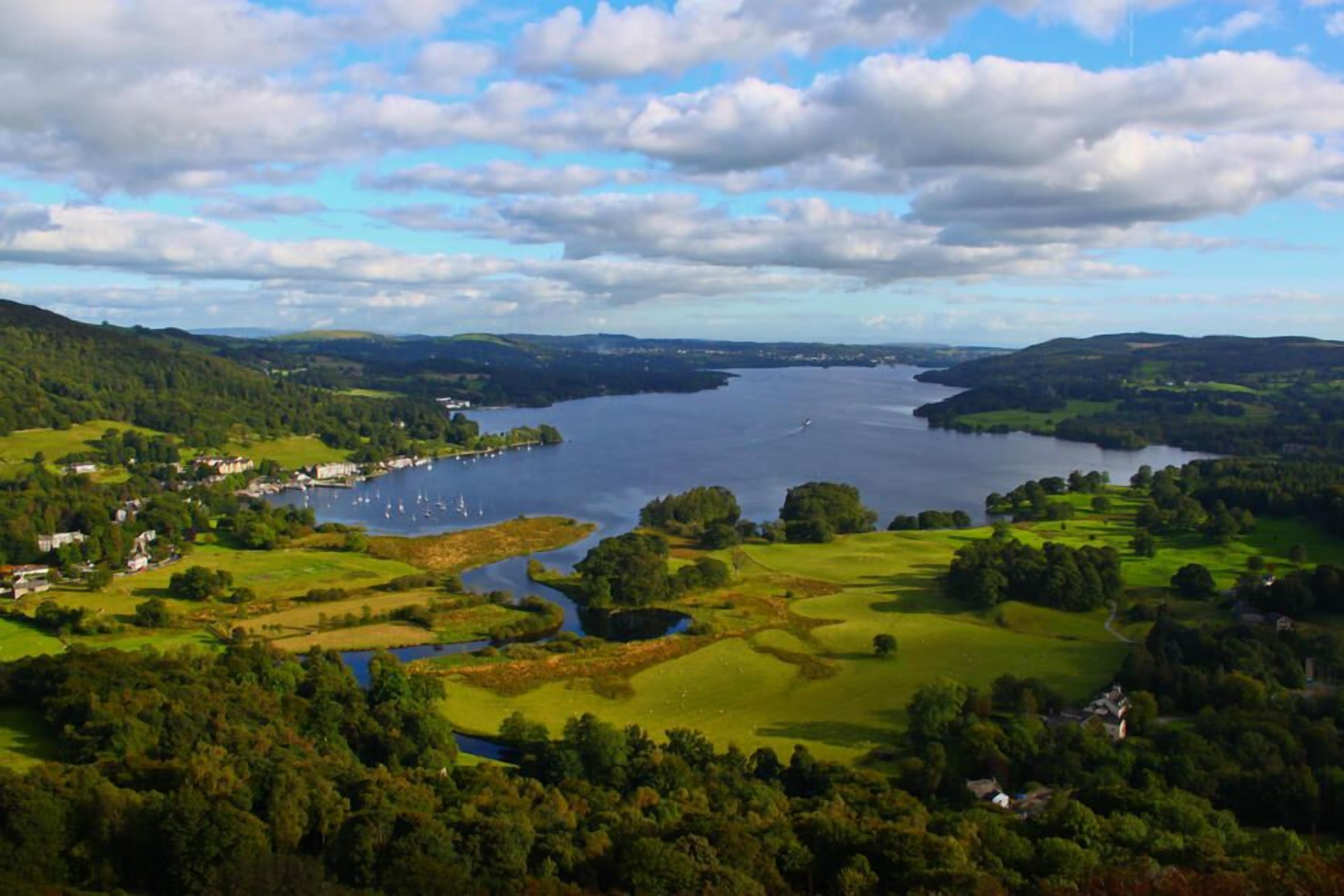 Une vue panoramique d’un lac entouré de collines verdoyantes et de quelques bâtiments dispersés.