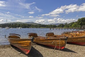 Holzboote liegen an einem Seeufer an, mit blauem Himmel und Bergen im Hintergrund.