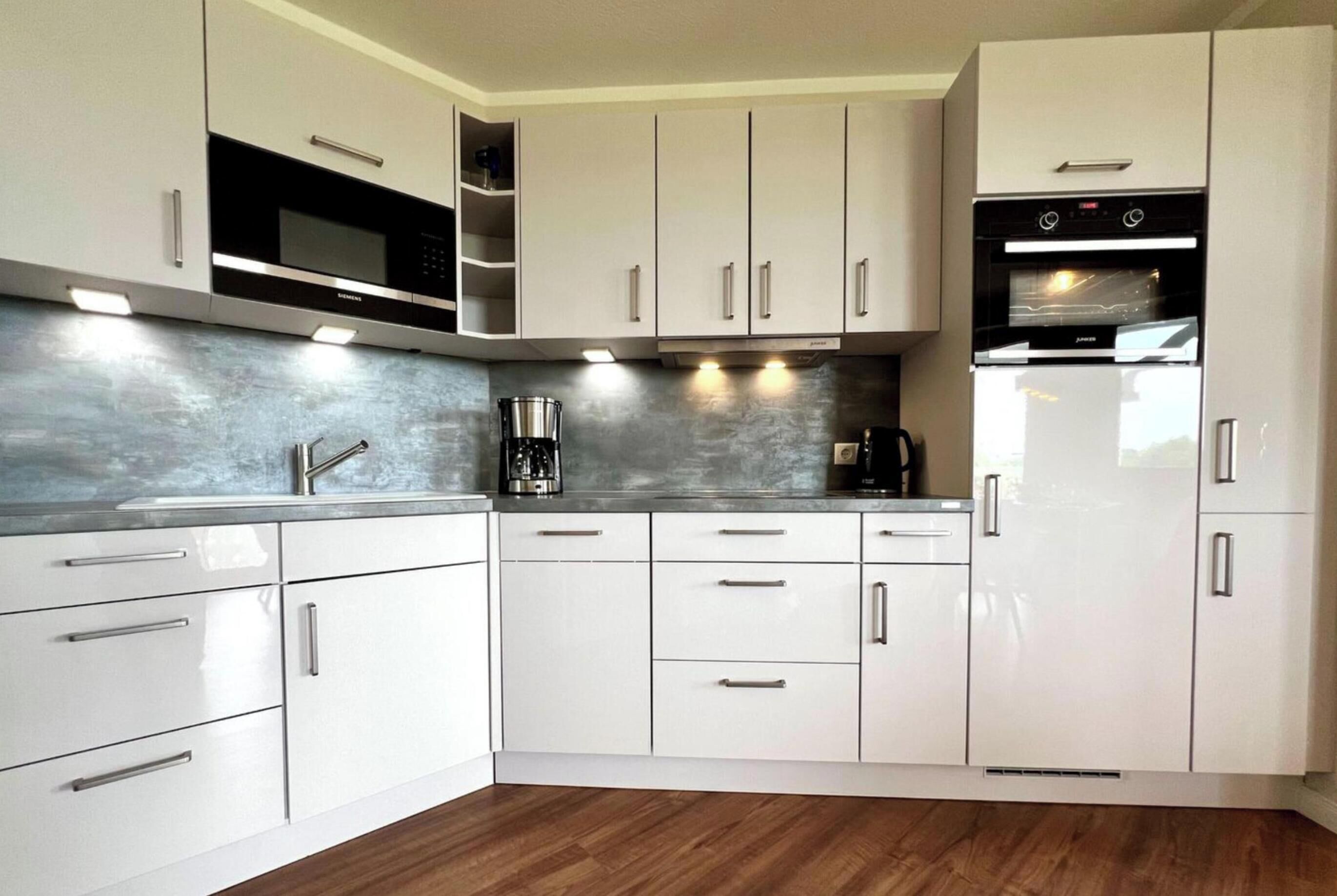 Una cocina moderna con armarios blancos, electrodomésticos de acero inoxidable y piso de madera.