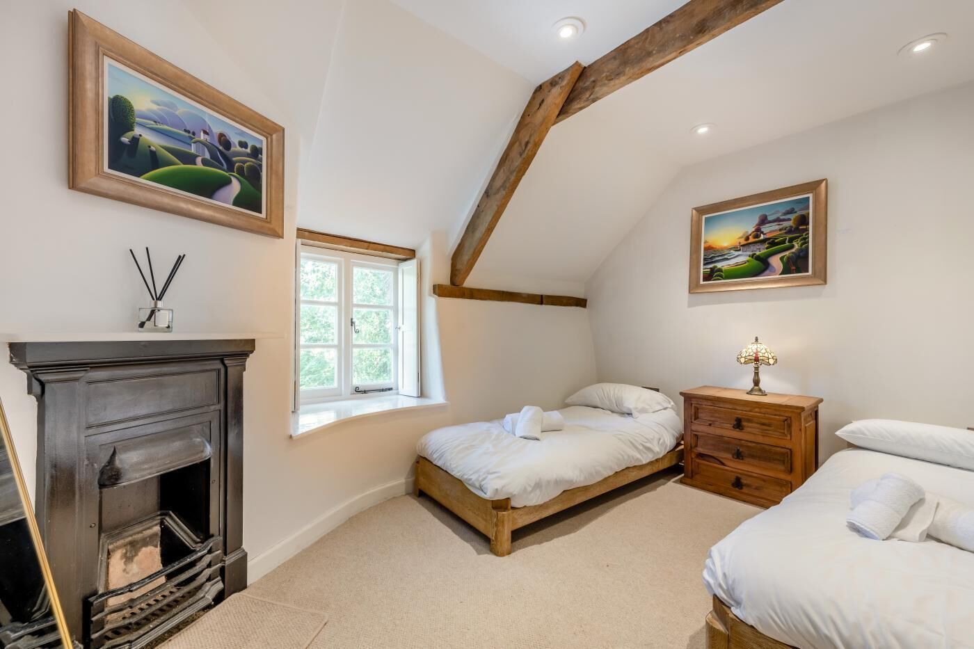 A bedroom with a fireplace, a bed, a nightstand, and two paintings.