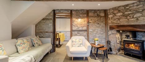 A cozy living room with a stone wall, a fireplace, a sofa, a chair, and a rug.