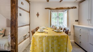 Un'area pranzo con tavolo apparecchiato per quattro, una finestra vista su piante e un trave in legno al soffitto.