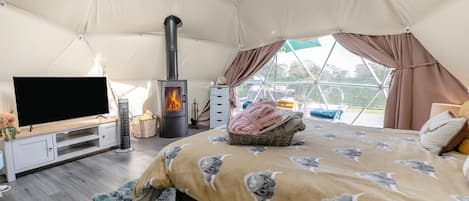 A tented room with a television, a fireplace, and a bed with a patterned blanket.