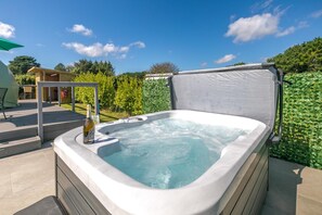 A hot tub with a bottle of champagne, surrounded by a wooden deck and a green hedge.