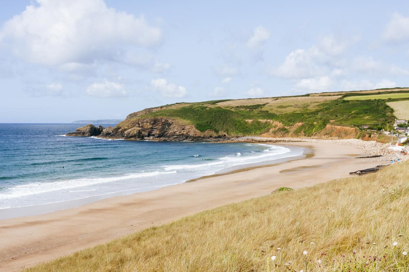 Paesaggio costiero con spiaggia sabbiosa, zone erbose e un promontorio roccioso.