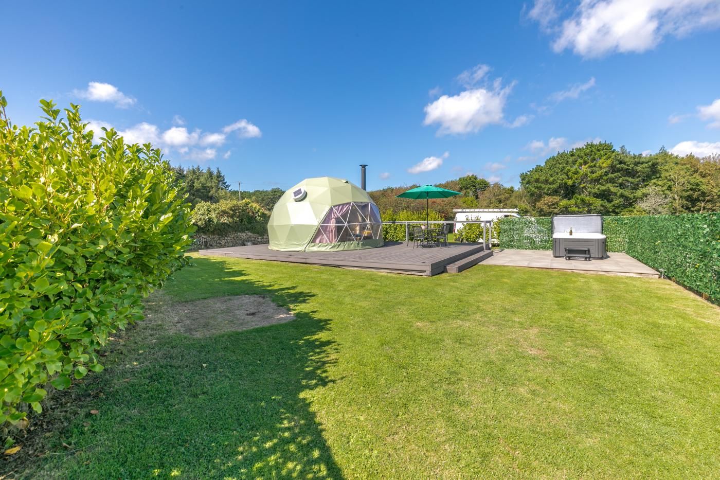 A green dome tent with a patio area, a hot tub, and a deck with outdoor furniture.