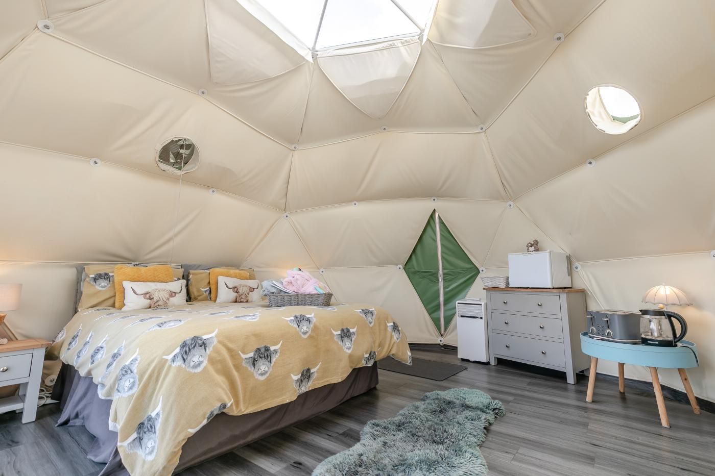 A tented room with a bed, a dresser, a lamp, and a coffee maker.