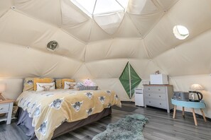A tented room with a bed, a dresser, a lamp, and a coffee maker.