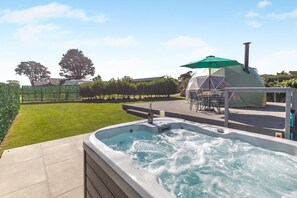 A hot tub with a table and chairs, a tent, and a fenced garden area.