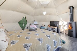 A cozy tented room with a bed, a television, a fireplace, and a small table with a lamp.