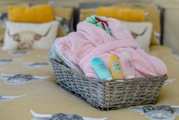Een rieten mand met een roze handdoek en twee flessen shampoo op een tafel met een tafelkleed met patroon.