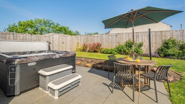 A backyard with a hot tub, a table with chairs, and an umbrella. - 1 Bed in Stewarton (oc-c44699) (Stewarton)