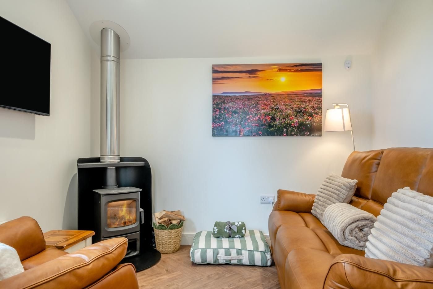 A cozy living room with a wood-burning stove, leather sofas, a flat-screen TV, and a sunset painting on the wall.