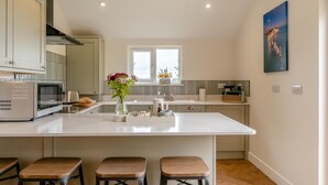 A modern kitchen with a central island, bar stools, a microwave, and a window. - 2 Bed in Adgestone (oc-i42801) (Brading)