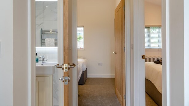 A bedroom with a bed, a window with blinds, a radiator, and a bathroom with a sink and mirror. - 2 Bed in Adgestone (oc-i42801) (Brading)
