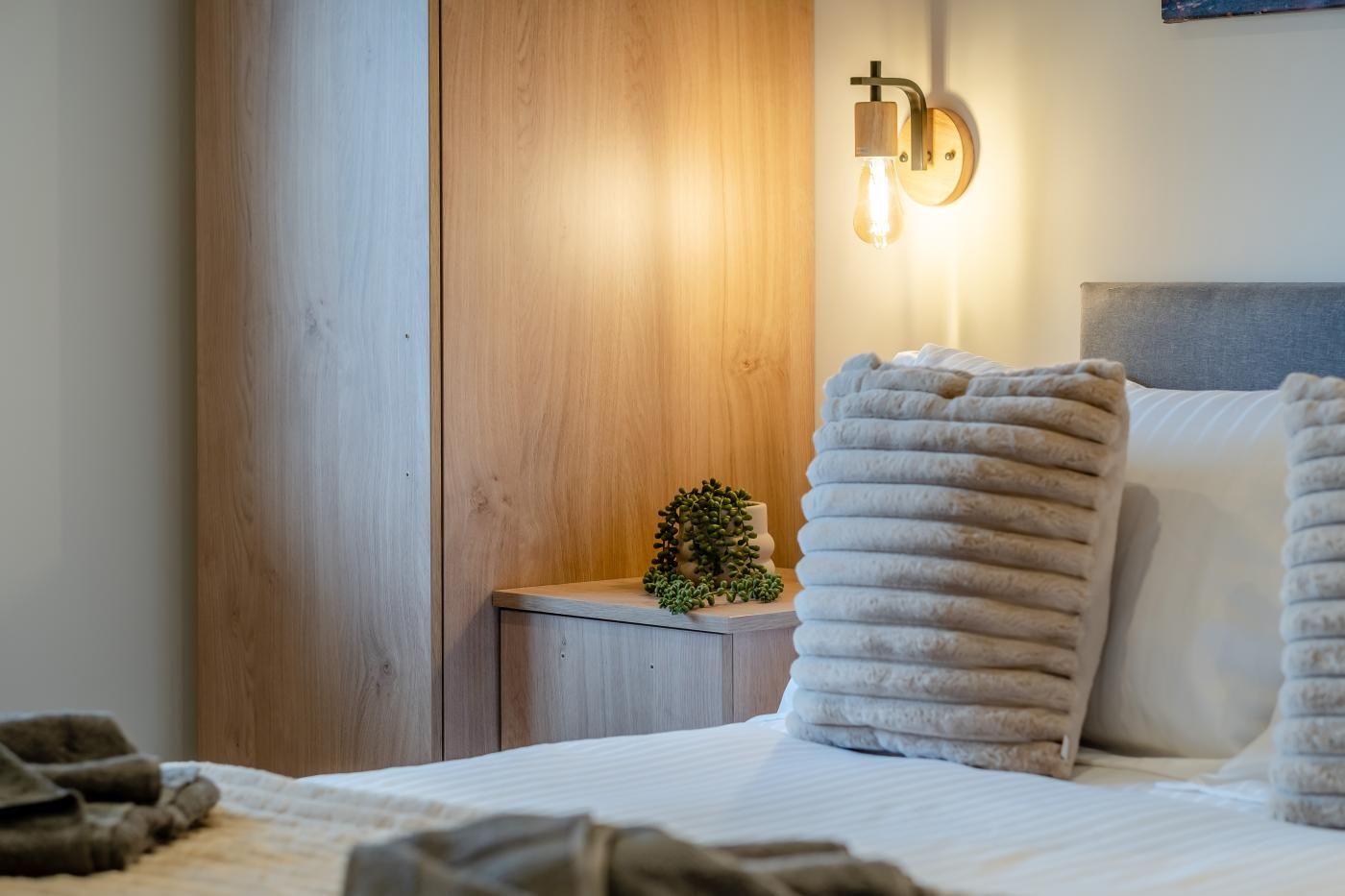 A neatly made bed with a white comforter, a grey headboard, and a stack of folded towels.