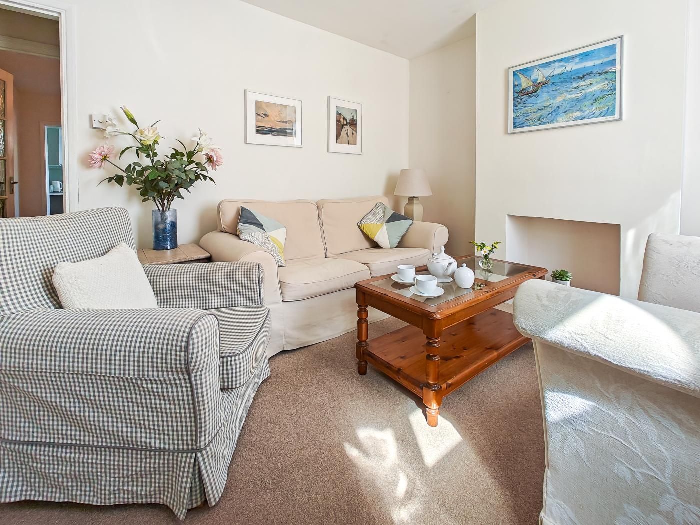 A living room with a beige sofa, a checkered armchair, a wooden coffee table with tea set, and a painting on the wall.