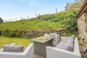A patio area with wicker furniture, a table with a tray of breakfast items, and a stone wall. - 2 Bed in Rhoslefain (oc-u44707) (Rhoslefain)
