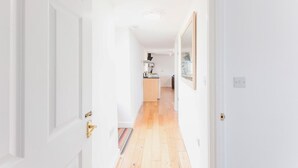 Un pasillo que conduce a una cocina con suelo de madera y paredes blancas.