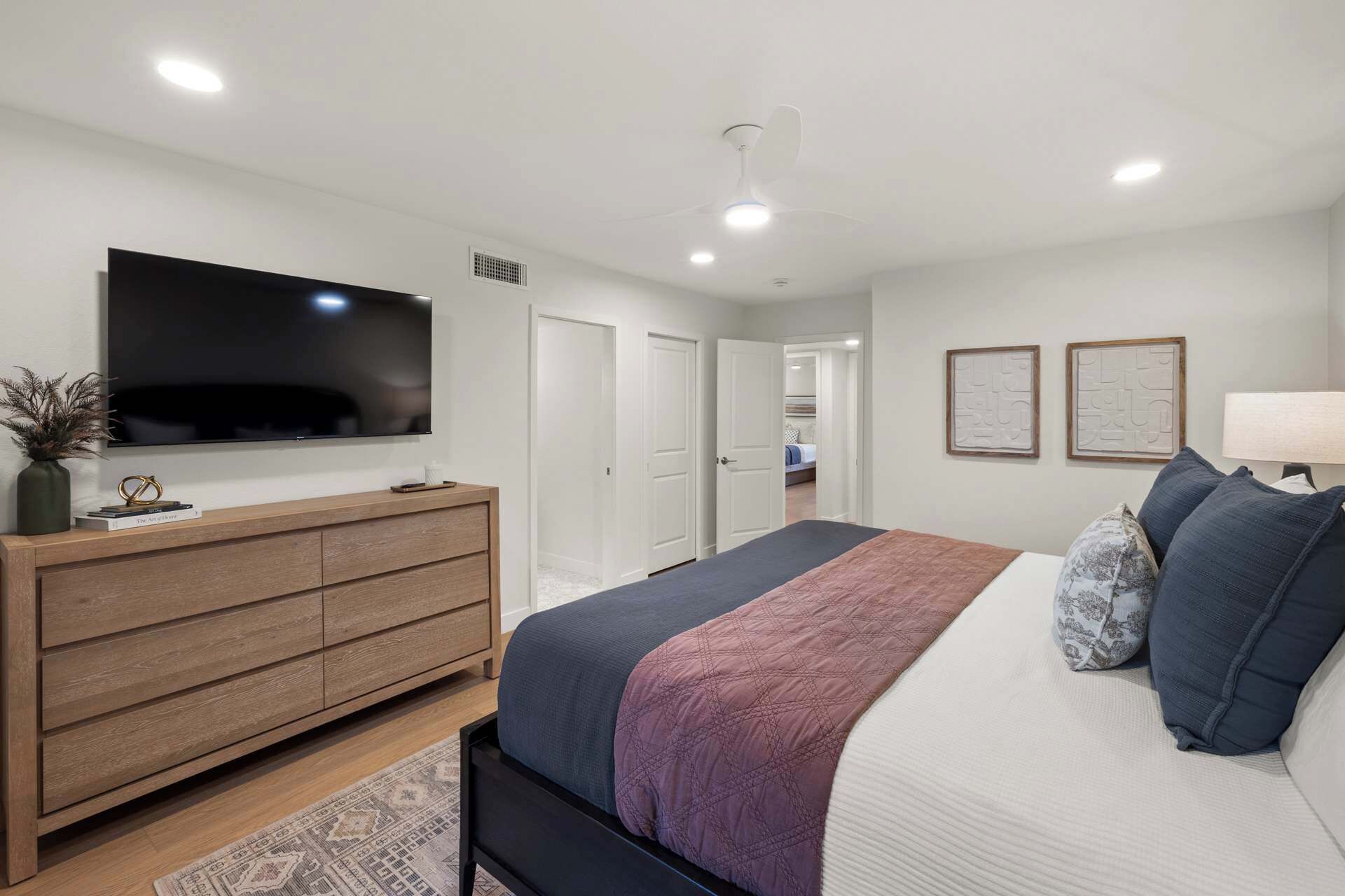 Un dormitorio con cama, televisor, cómoda y una puerta que da a otra habitación.