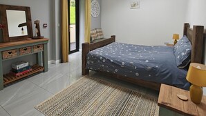 Ein Schlafzimmer mit Dachfenster, einem Bett, einem Nachttisch, einem Spiegel und einem Regal mit Spielen, sowie einem gemusterten Teppich.