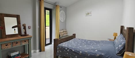 A bedroom with a skylight, a bed, a bedside table, a nightstand, a mirror, a shelf with games, and a patterned rug.