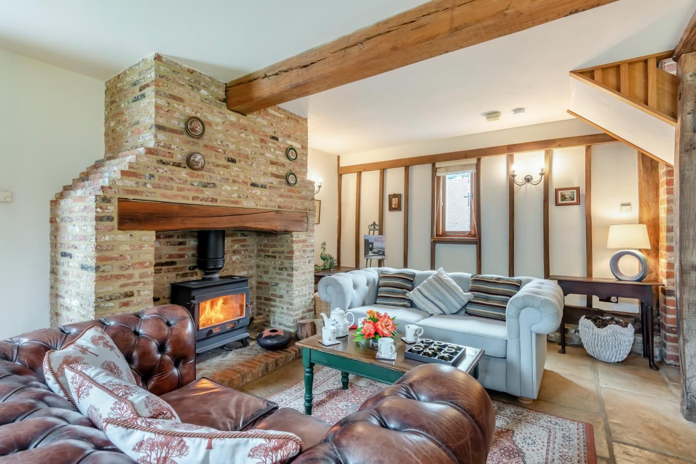 A cozy living room with a brick fireplace, leather sofas, and a wooden ceiling.