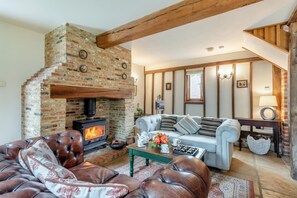 A cozy living room with a brick fireplace, leather sofas, and a wooden ceiling.