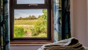 A window with a view of a green landscape, curtains, and a folded blanket on a bed. - 3 Bed in Studland (oc-o42812) (Studland)