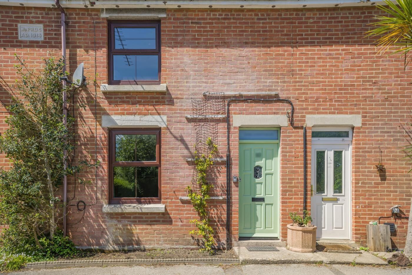 A two-story brick house with a green door, a satellite dish, and a small window.