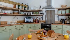 A kitchen with wooden shelves, a microwave, a stove, and a dining table set with breakfast. - 2 Bed in Hartest (oc-w42830) (Hartest)