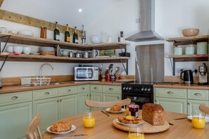 A kitchen with wooden shelves, a microwave, a stove, and a dining table set with breakfast. - 2 Bed in Hartest (oc-w42830) (Hartest)
